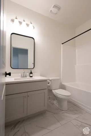 Bathroom featuring neutral-toned cabinetry, solid surface countertop, rectangular mirror with a black frame, and large-format tile flooring