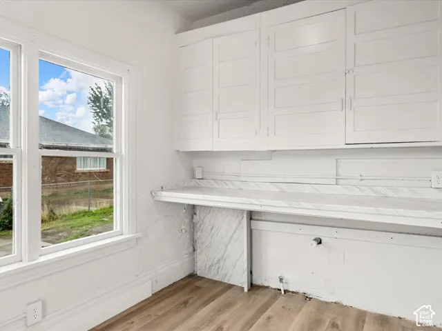 Wall-mounted white cabinetry, stone-patterned countertop, wood-finish flooring, and large window with exterior exposure