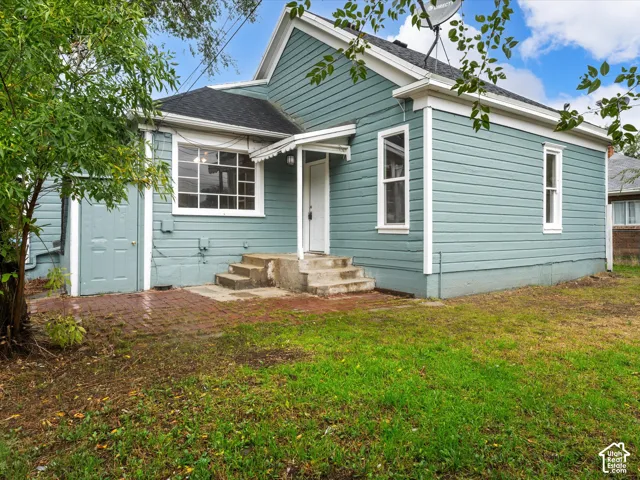 Exterior featuring blue lap siding, white trim, a shingled roof, a brick patio, and concrete entry steps