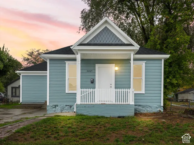 Exterior featuring blue lap siding, a front porch with a white picket railing, shingled gable roof with diamond pattern decorative siding, and a stone foundation