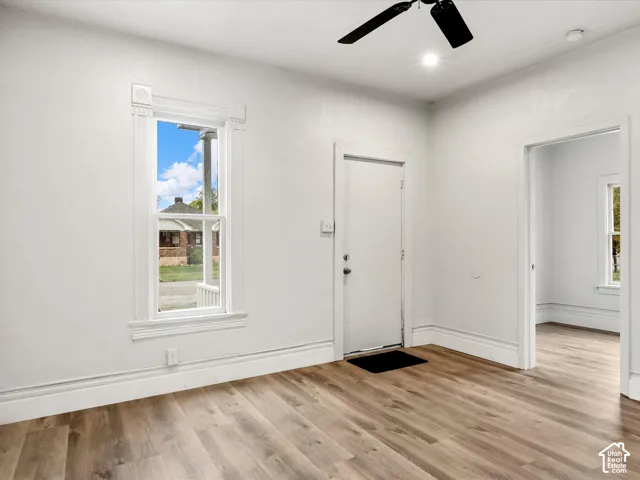 Interior featuring wood-finish flooring, white walls, a ceiling fan, and window casing with decorative corner blocks