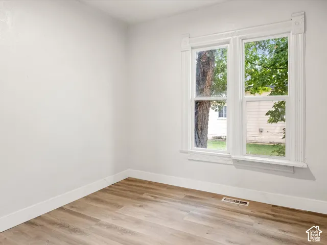 Room featuring wood-finish flooring, neutral wall paint, and a window framed by detailed woodwork with corner block molding