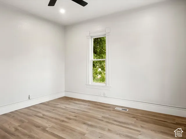 Room interior featuring wood-finish flooring, white walls, and a single-hung window with decorative millwork trim