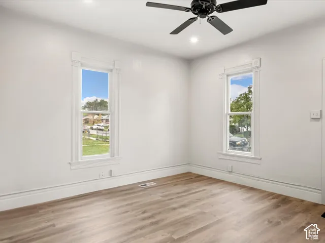 Room featuring wood-finish flooring, two windows with architectural trim casing, and a black ceiling fan