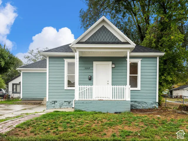 Exterior featuring blue horizontal siding, a covered front porch with a white picket railing, a gable roof with decorative diamond-patterned shingle detailing, and a stone foundation