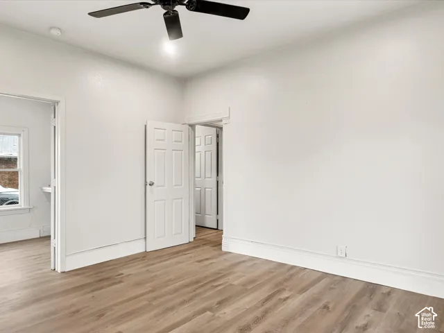 Room featuring wood-finish flooring, white walls, and a ceiling-mounted fan with light fixture