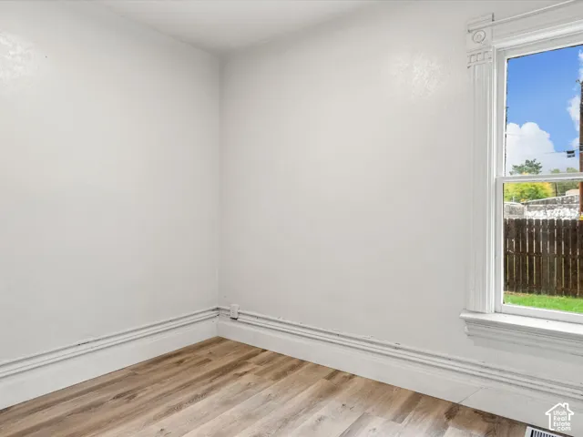 Room featuring wood-finish flooring, white walls, and a window with decorative colonial-style casing