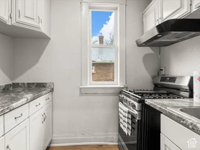 Kitchen featuring white cabinetry, stone-finish countertops, stainless steel gas range, and wall-mounted stainless steel exhaust hood