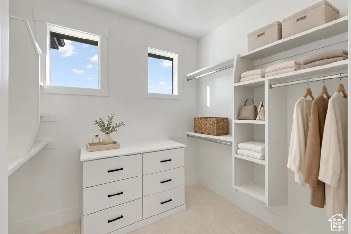 Walk-in closet featuring custom white built-in shelving, hanging rods, an integrated dresser with matte black hardware, and two windows