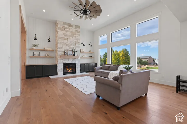 Living area featuring wood-finish flooring, floor-to-ceiling windows, stone-faced fireplace with a wood mantel, built-in cabinetry, and a statement windmill-style ceiling fan