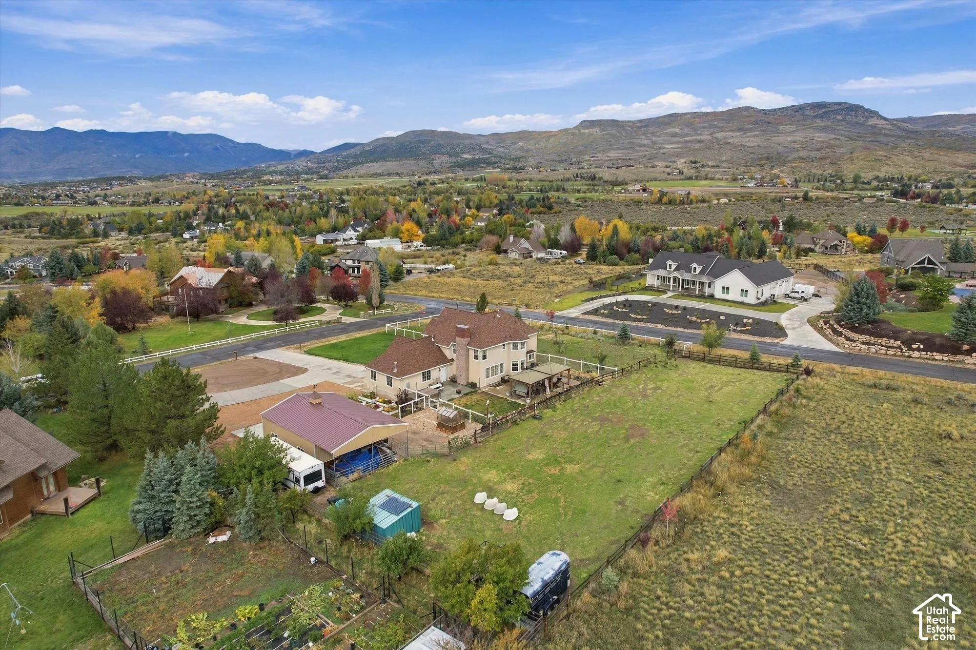 Aerial perspective featuring an expansive lot, a detached metal-roofed outbuilding, fenced perimeter, and mountainous horizon