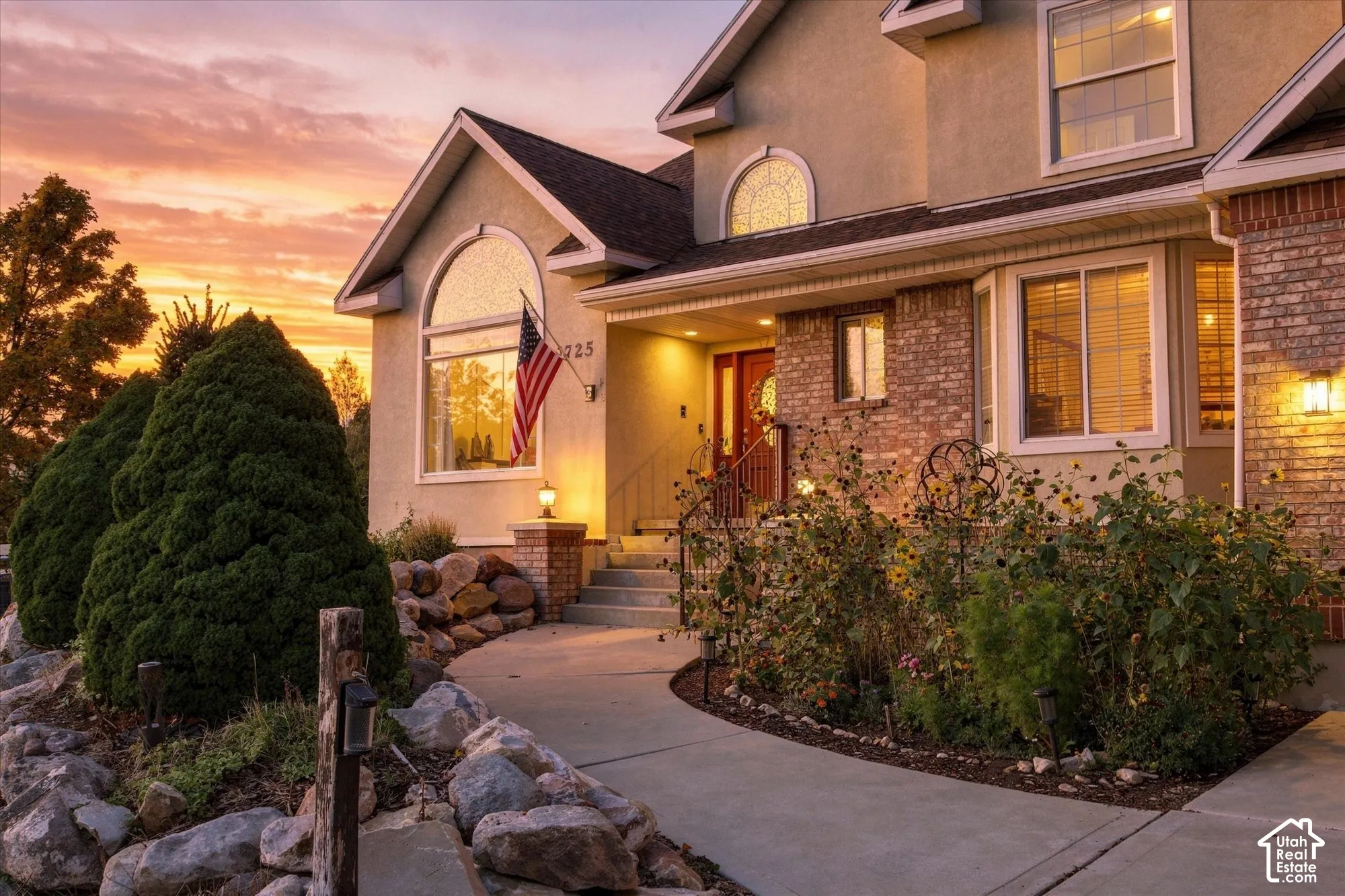 Stucco and brick facade featuring arched windows, a concrete walkway, and stone landscaping accents