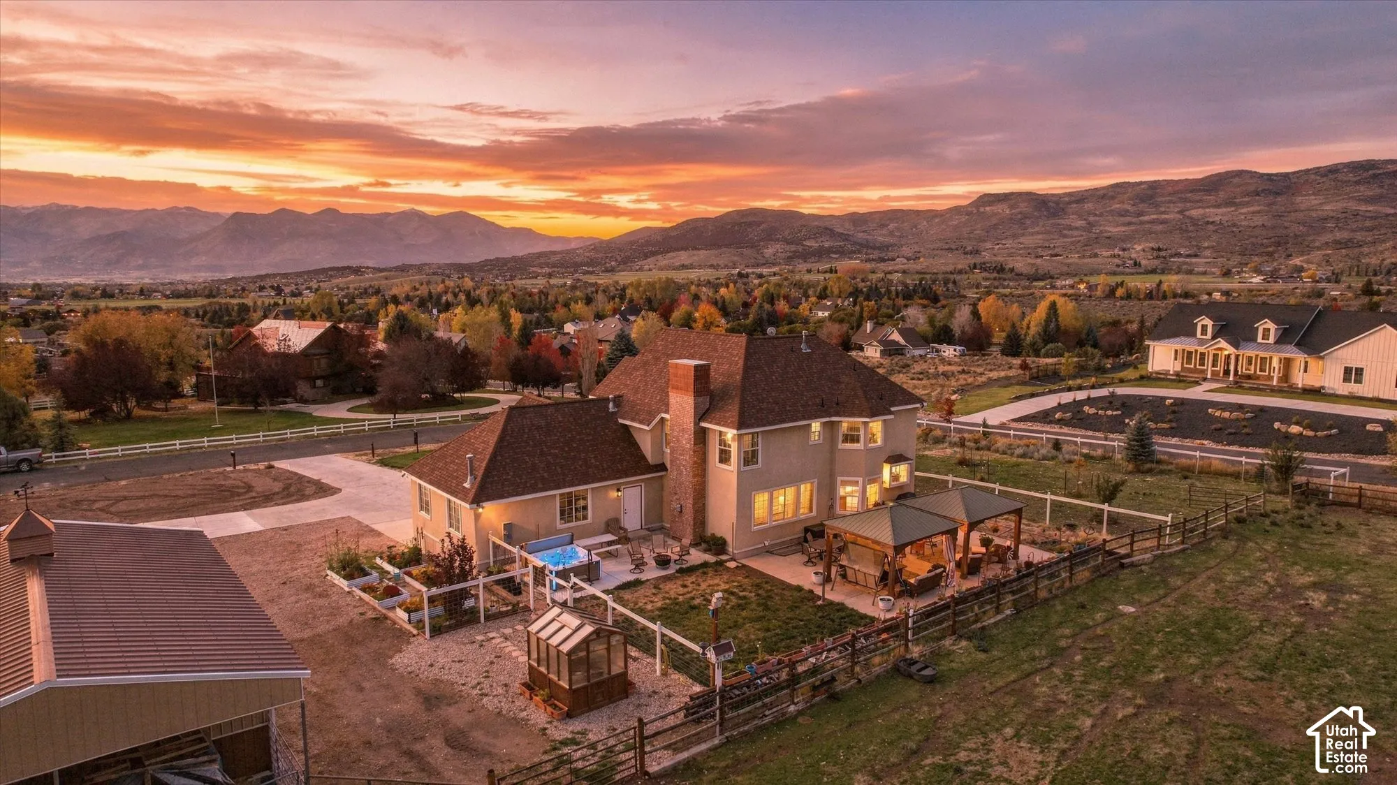 Aerial perspective of a multi-story residence featuring a brick chimney, a concrete patio with a covered structure, an enclosed greenhouse, and mountain scenery