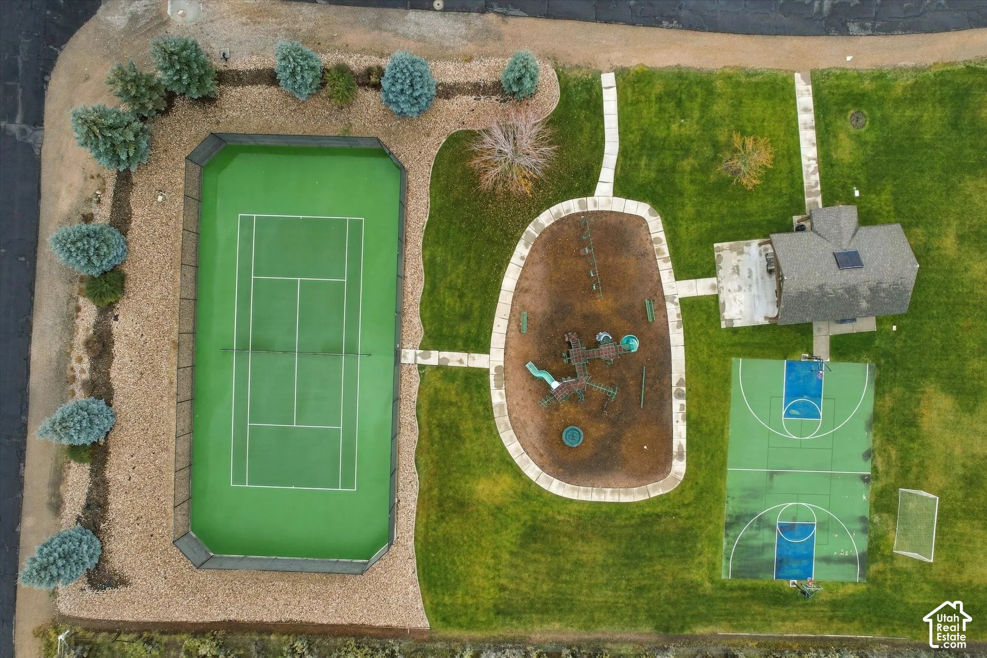 Recreational grounds featuring a fenced tennis court, a basketball court, a playground area, and a structure with a shingled roof