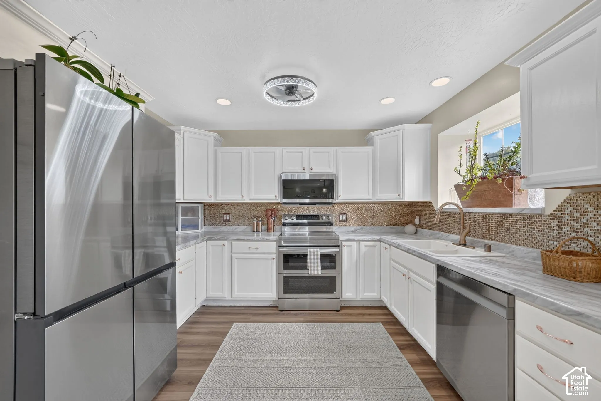 Kitchen featuring white cabinetry, stainless steel appliances, wood-finish flooring, mosaic tile backsplash, and stone-finish countertops