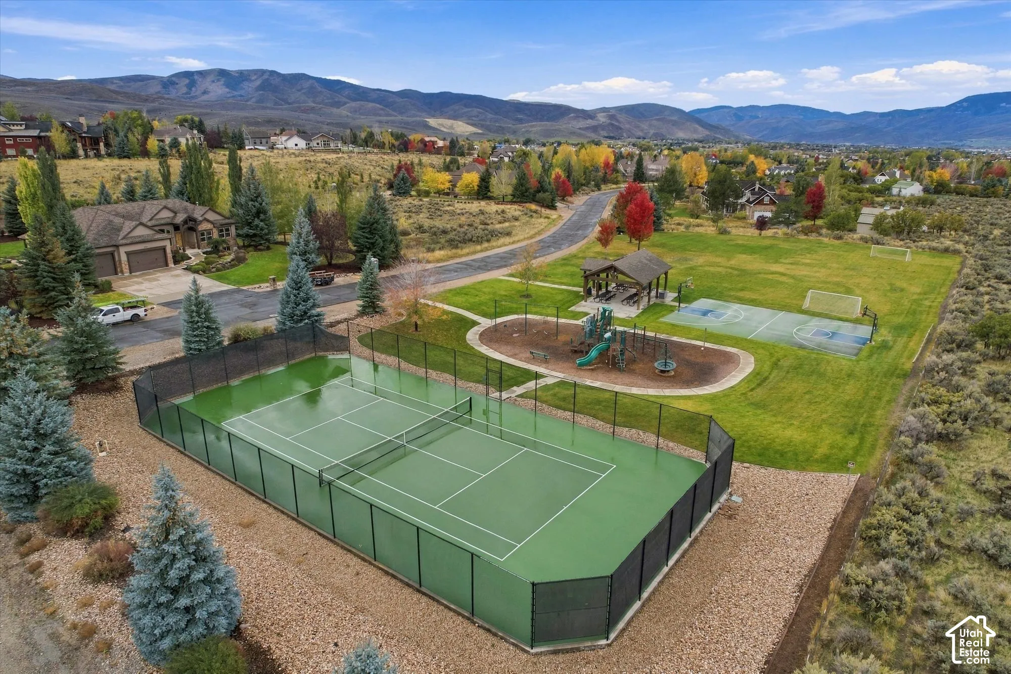 Fenced tennis court, multi-purpose sport court, covered pavilion, play structure, and expansive grounds featuring mountain terrain