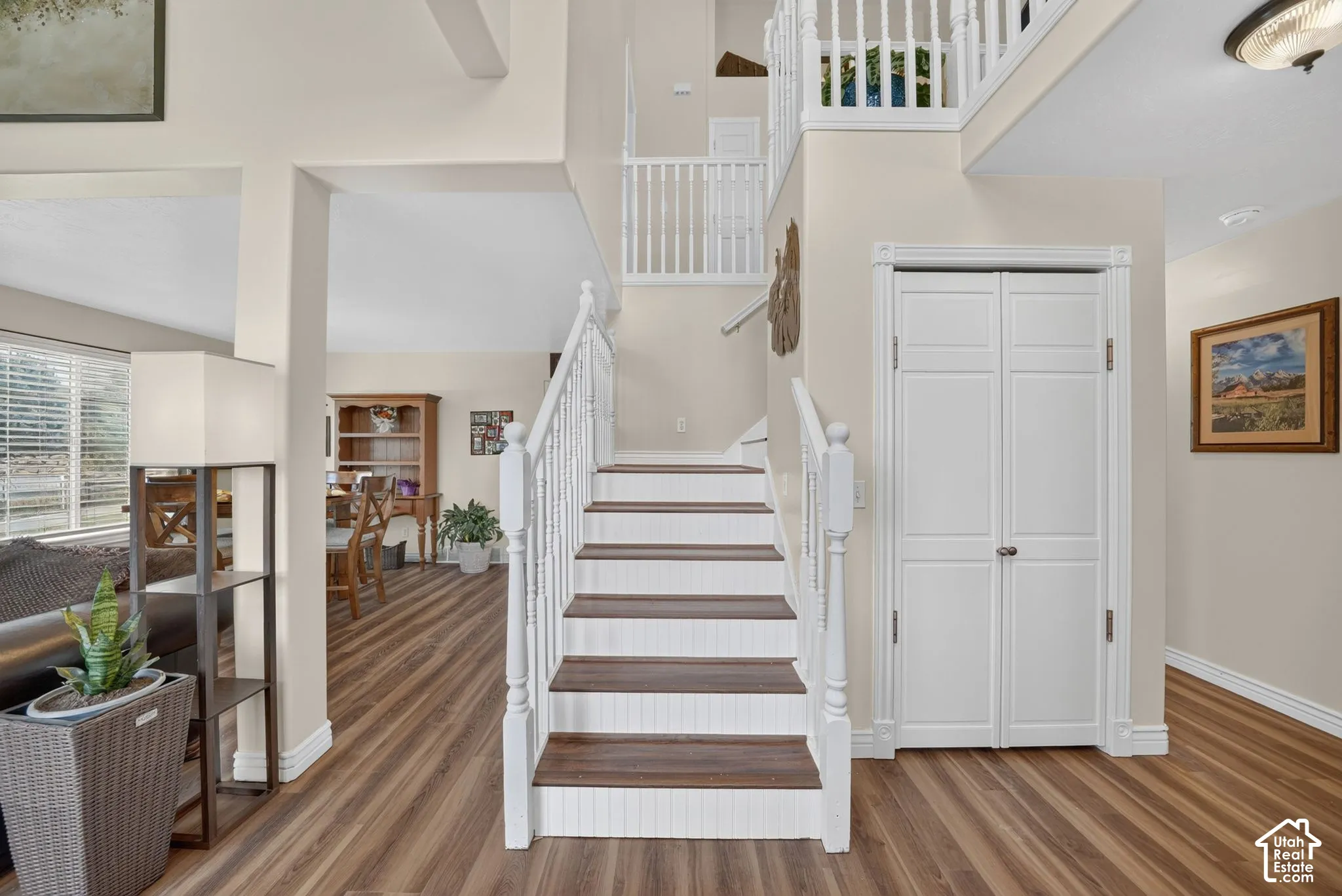 Foyer featuring wood-finish flooring, a staircase with white balusters and wood-tone treads, high ceilings, and a double-door closet with millwork trim