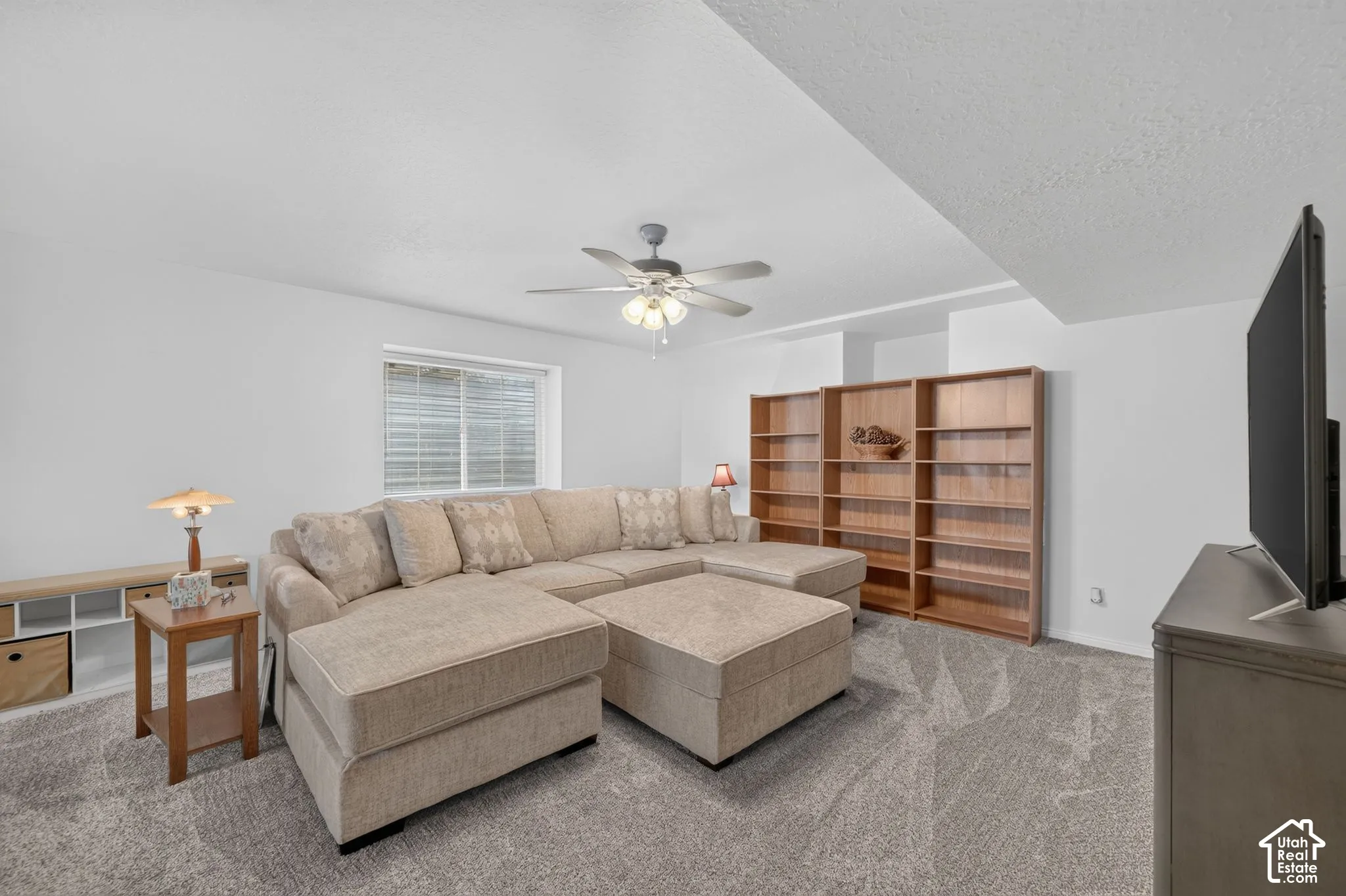 Neutral-toned carpeting, wood-finish built-in shelving, and a ceiling fan with integrated lighting
