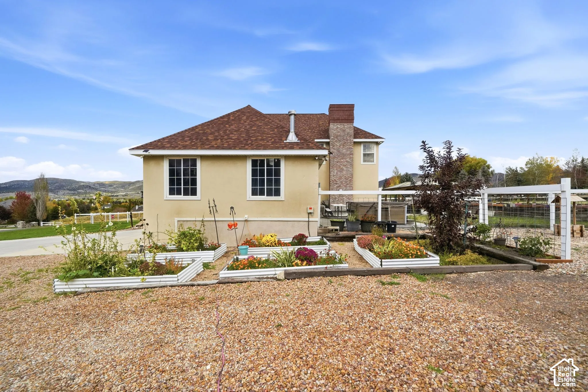 Stucco exterior featuring a brick chimney, multiple raised metal garden beds, and mountain scenery