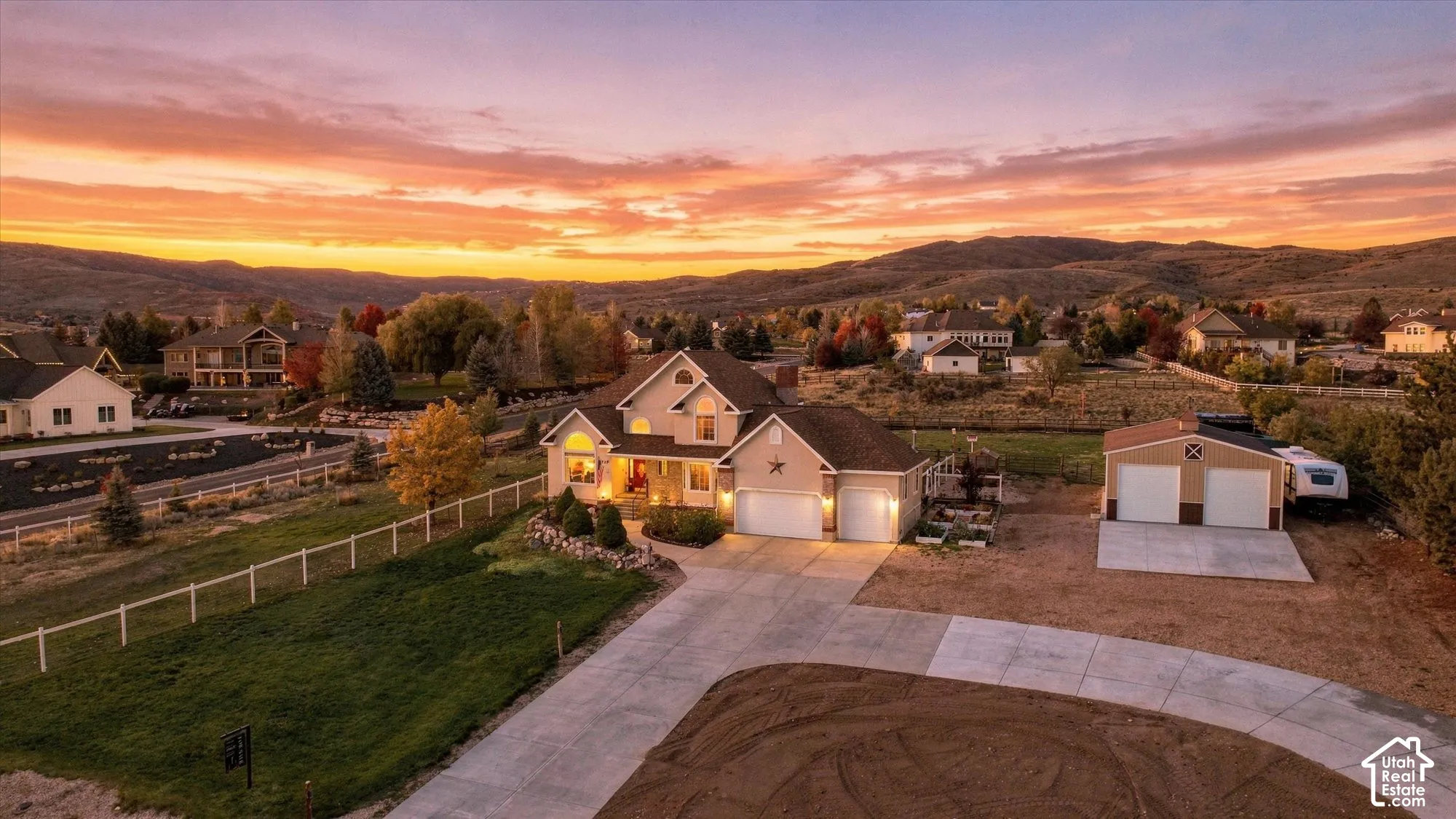 Multi-level residence featuring a pitched shingle roof, attached three-car garage, secondary detached two-car garage, and expansive concrete driveway set against a mountainous backdrop