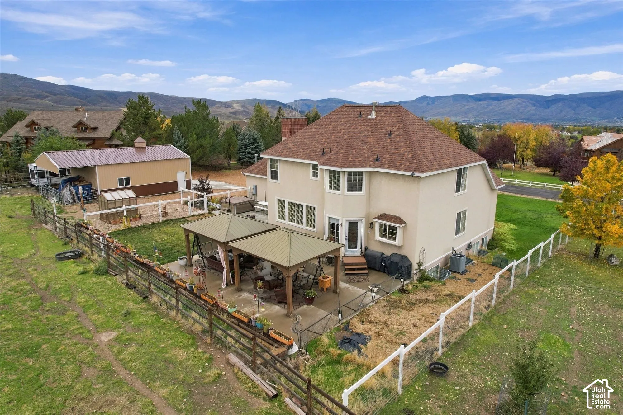 Multi-story residence featuring a stucco exterior, expansive lawn, detached outbuilding, fenced perimeter, and permanent metal-frame patio cover