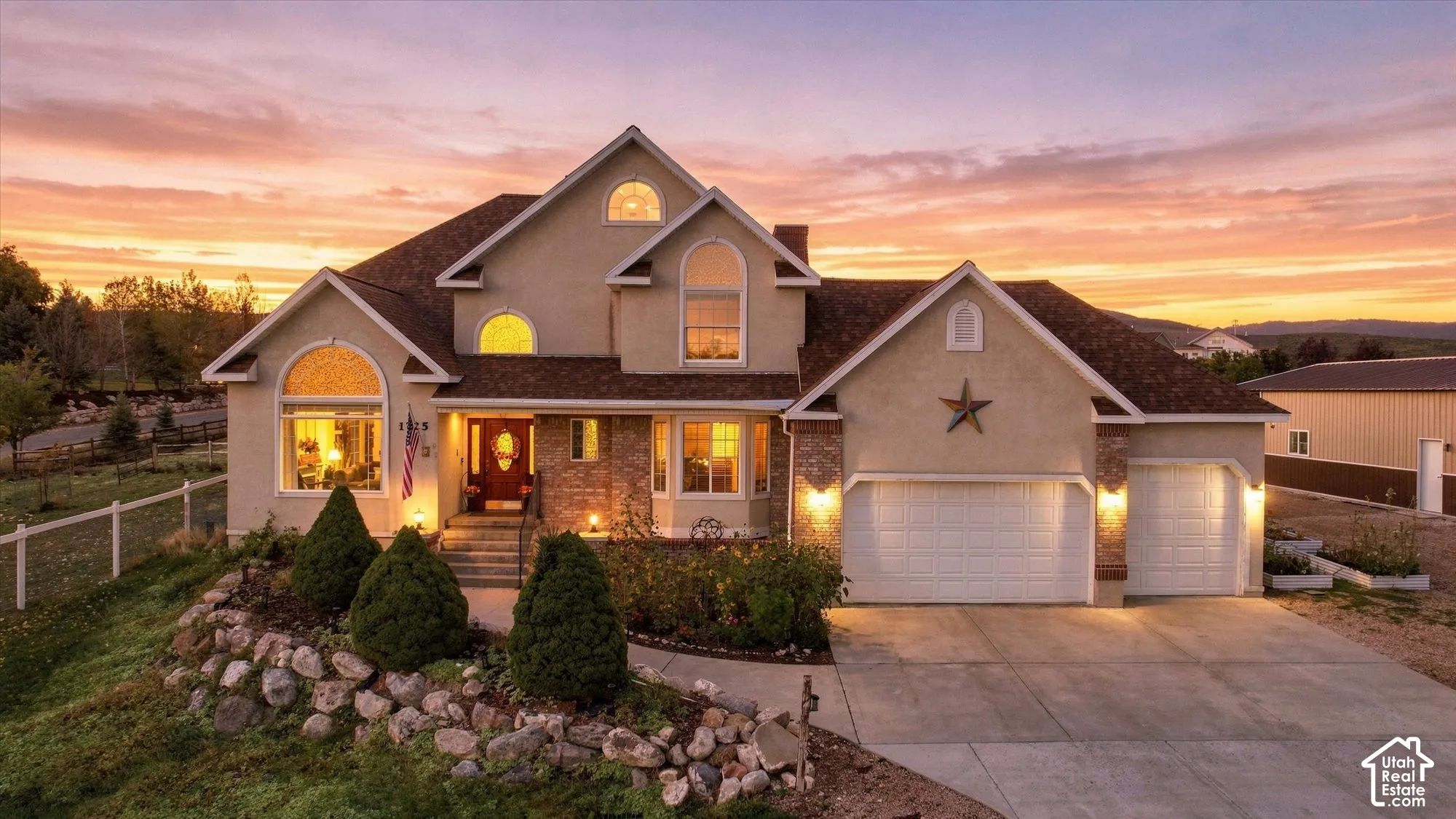 Multi-level stucco exterior featuring stone masonry accents, a three-car garage, arched windows, and a landscaped rock garden