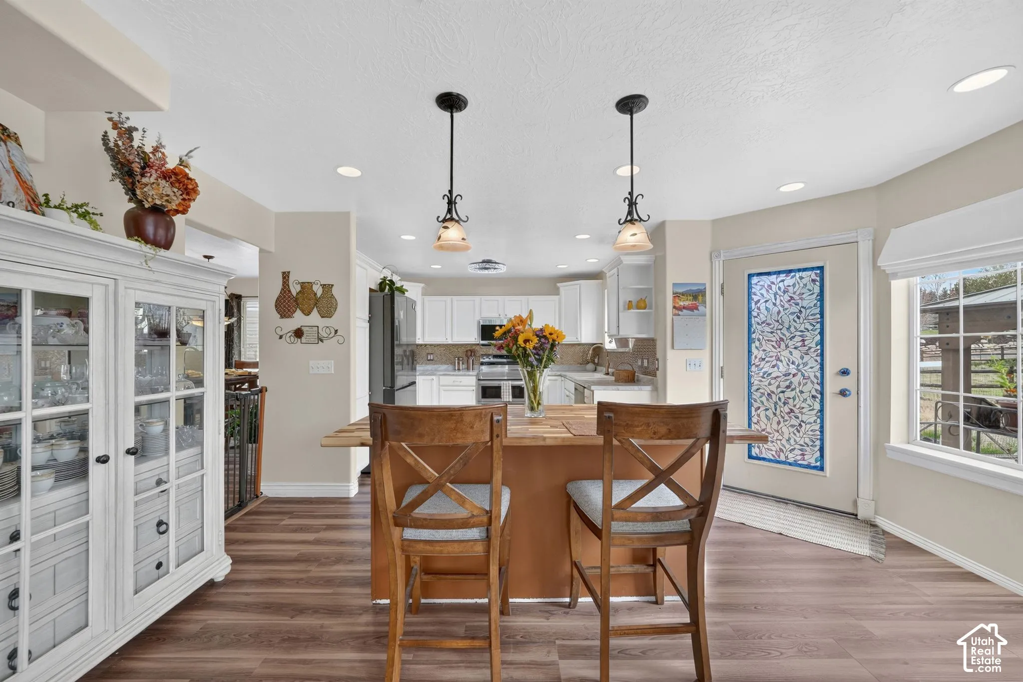 Kitchen featuring white cabinetry, wood-finish flooring, dual overhead pendant lighting, recessed ceiling lights, and an exterior door with decorative glass paneling