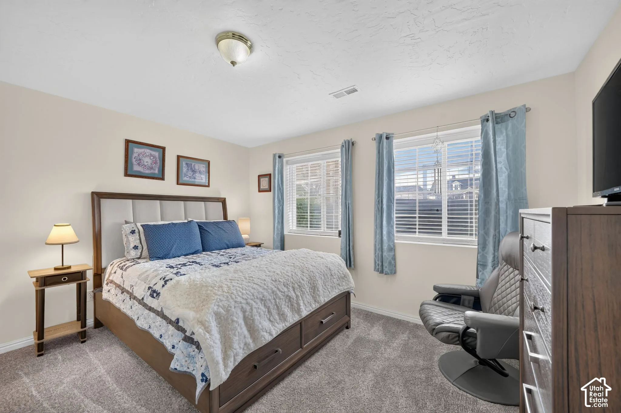 Neutral-toned interior space featuring neutral wall paint, plush carpeting, two windows with horizontal blinds, and a central ceiling-mounted light fixture
