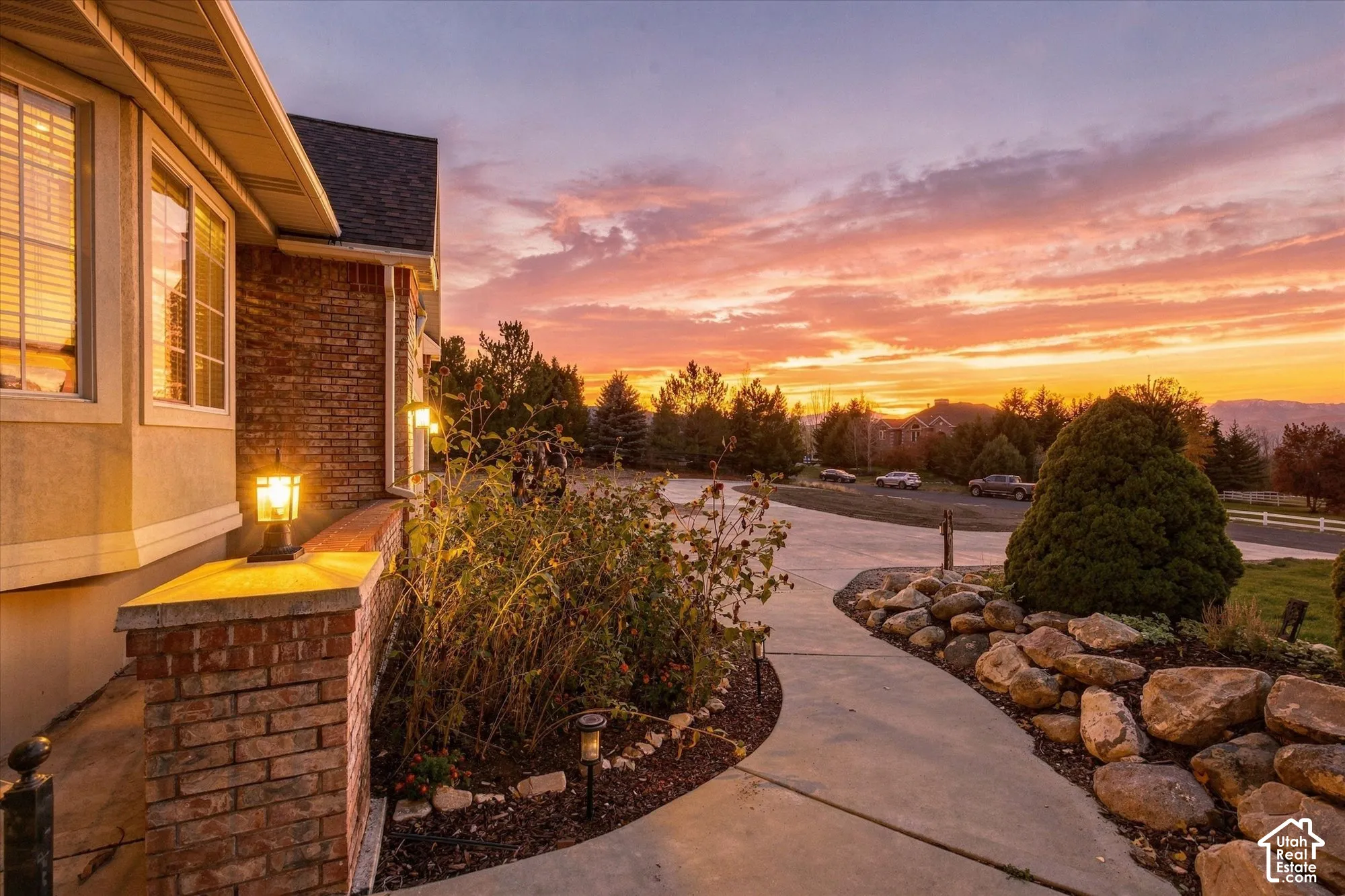 Exterior facade featuring brick masonry, multi-pane windows, stone hardscaping, concrete walkway, and built-in wall-mounted lighting