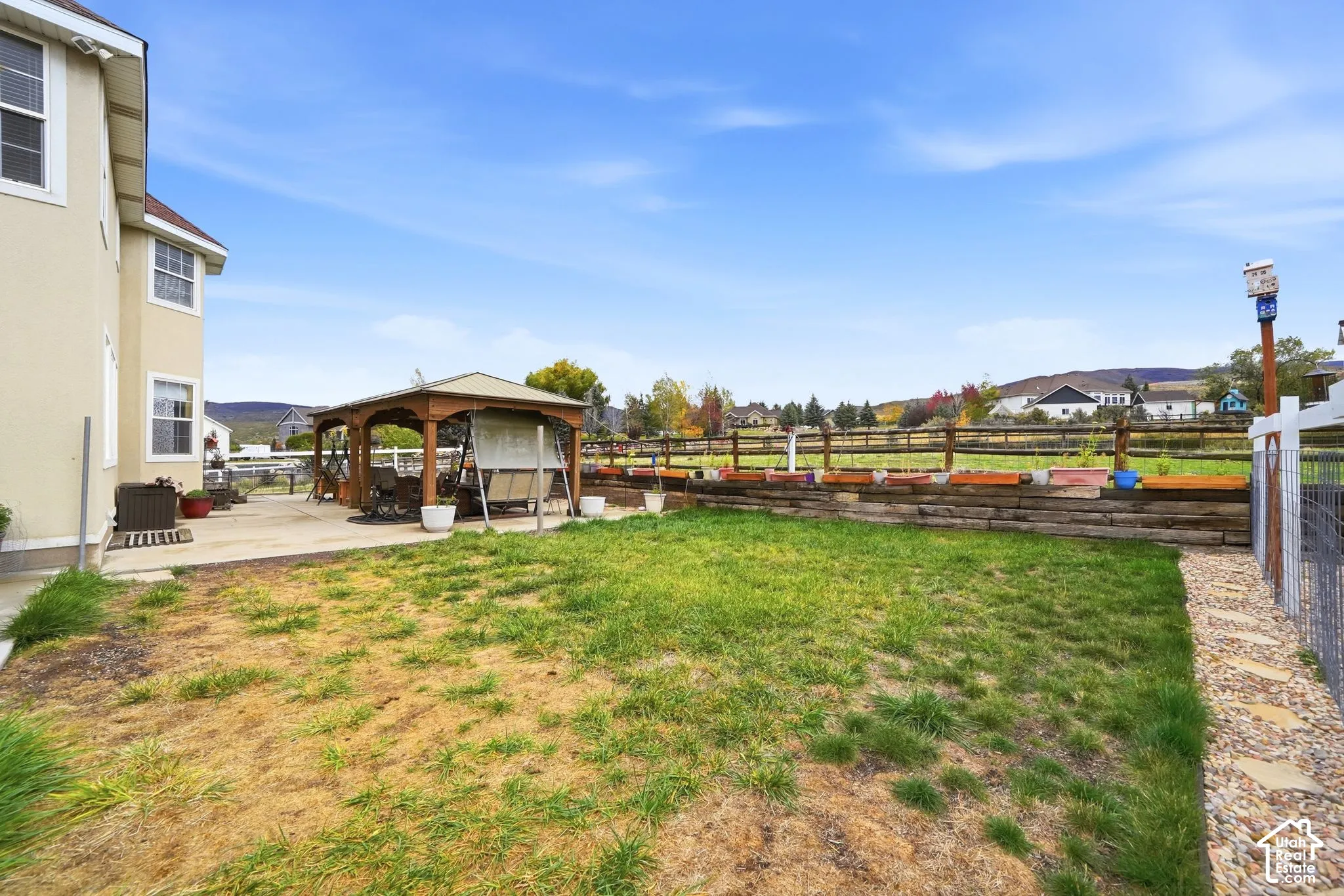 Fenced backyard featuring a covered wood-frame gazebo, concrete patio, tiered timber retaining wall, and mountain backdrop