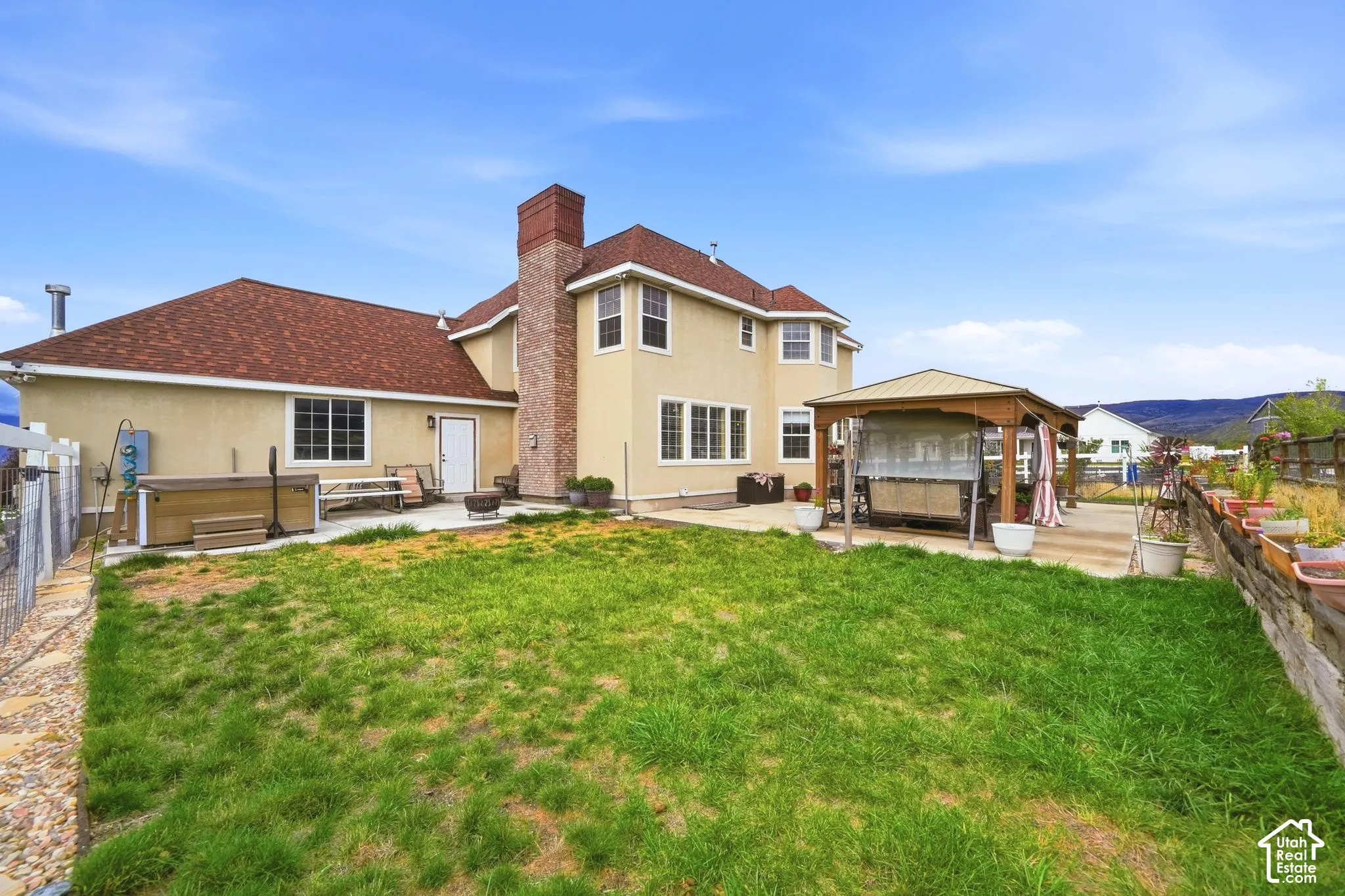 Rear exterior featuring a concrete patio, brick chimney, detached wooden gazebo, and metal perimeter fencing