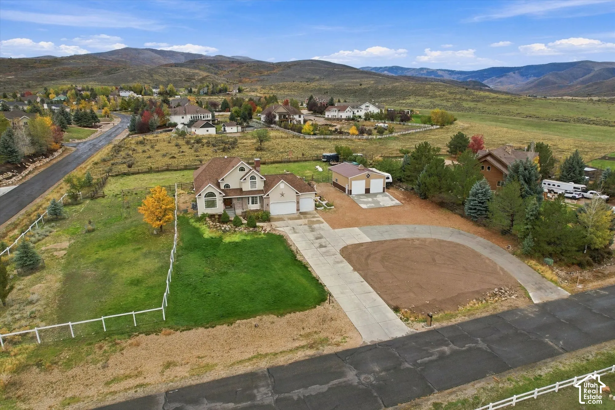Aerial view featuring a multi-level residence, detached two-car garage, expansive lot with fenced perimeter, and mountainous horizon