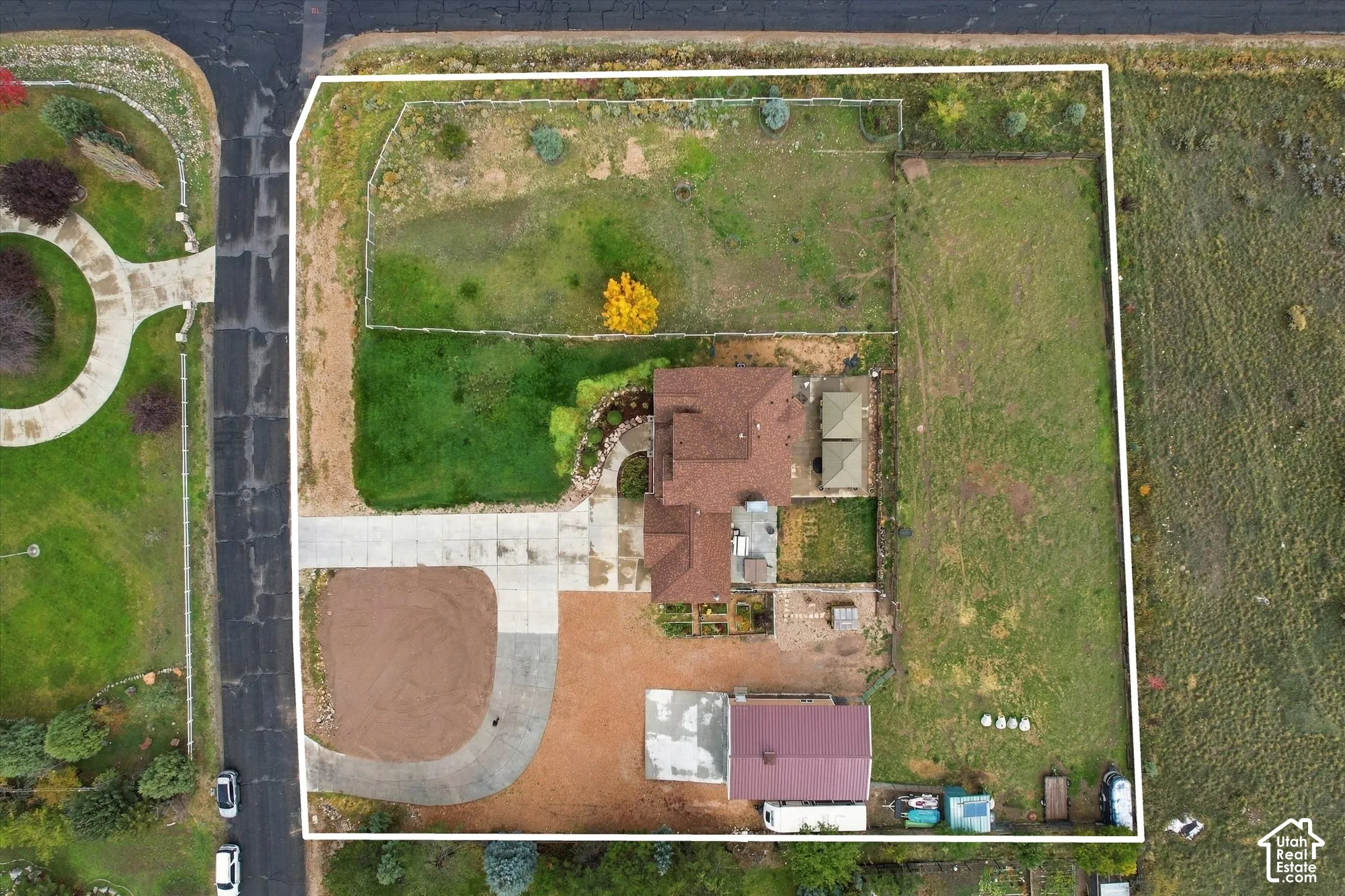 Aerial perspective of a sprawling lot featuring a multi-section roofline, expansive grounds, a concrete driveway, and dedicated hardscaped areas