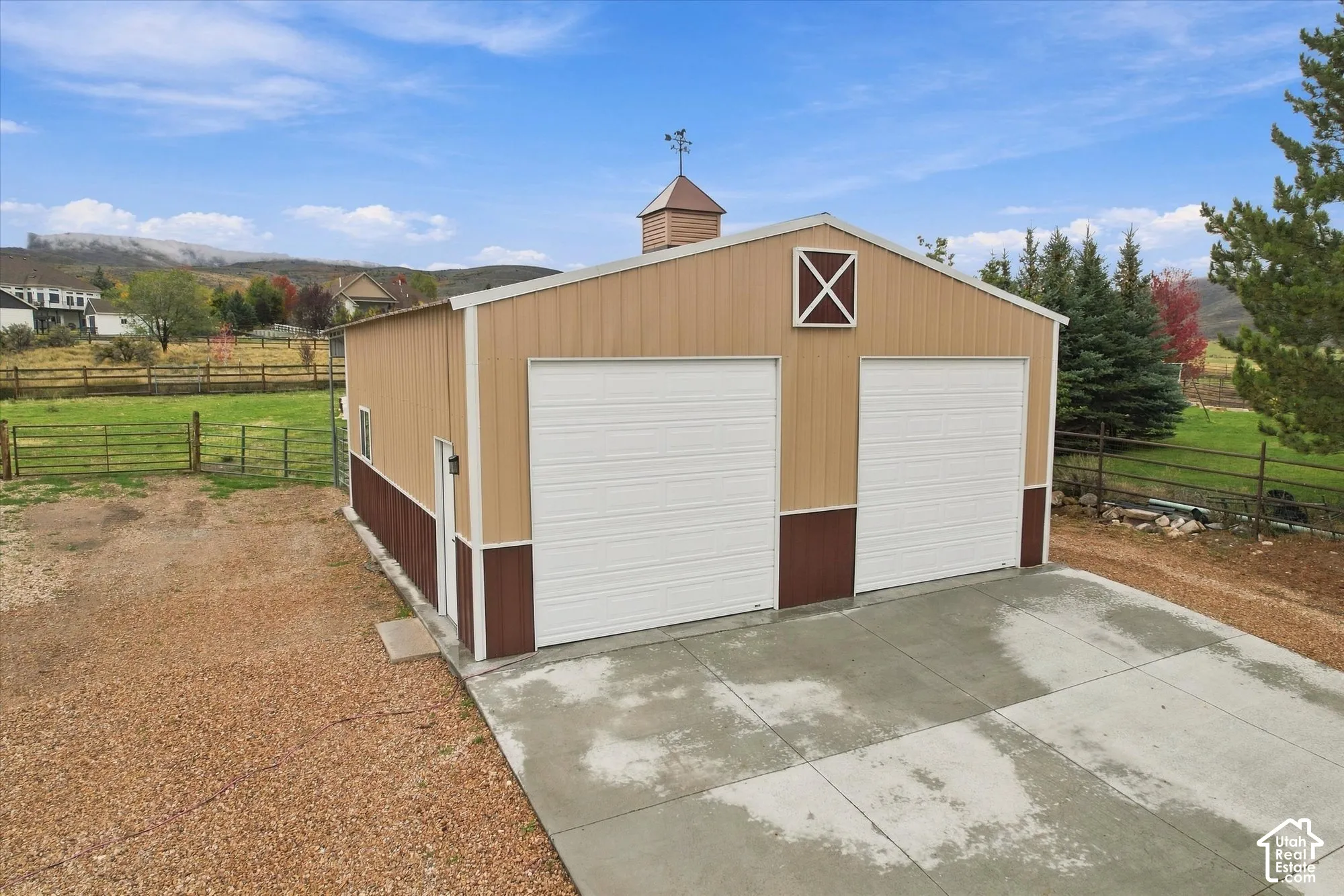 Detached outbuilding featuring a two-car metal garage, concrete apron, gable roofline with a cupola, and dual roll-up doors
