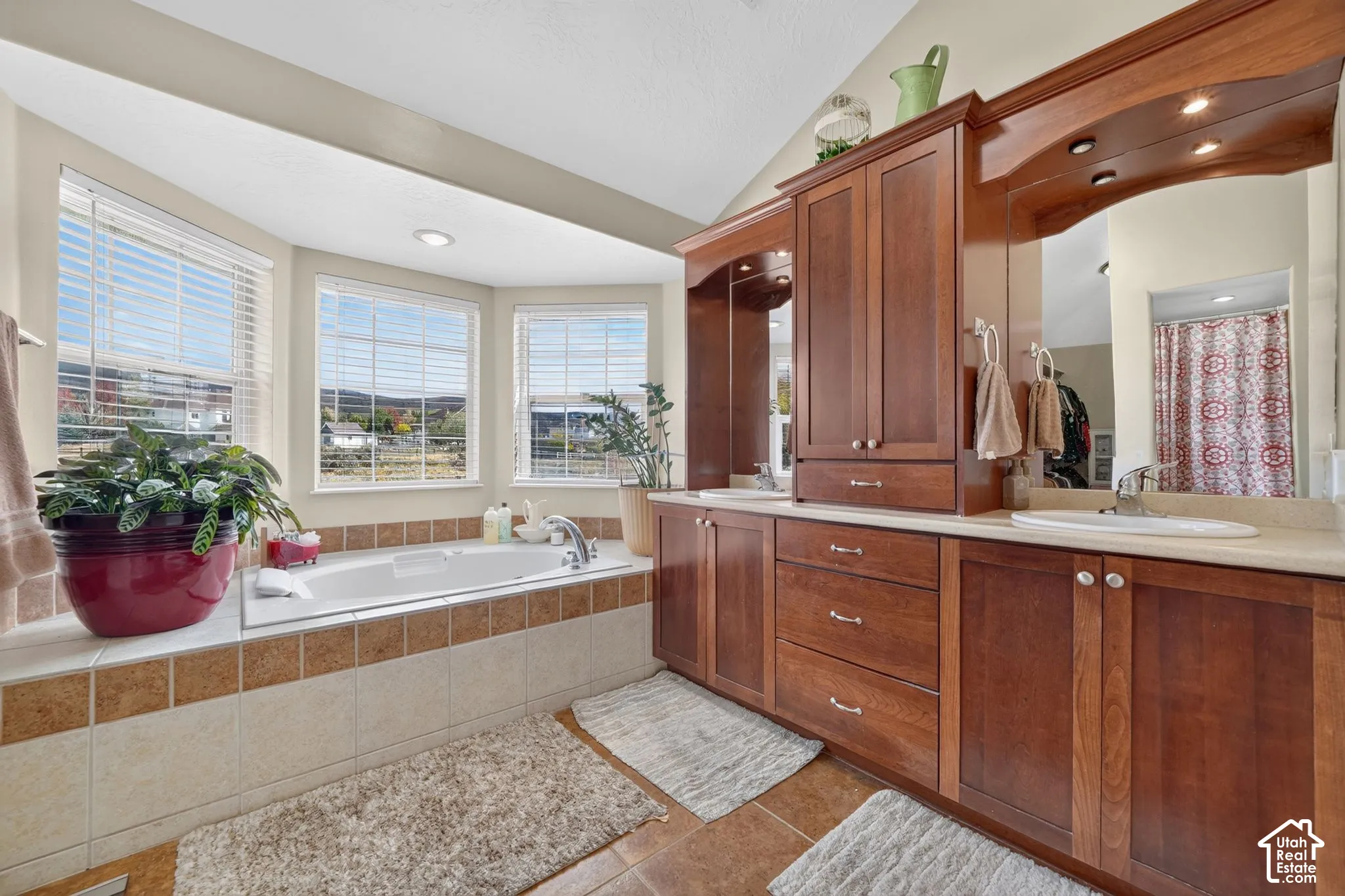 Built-in wooden cabinetry featuring a dual-sink vanity, tile-surround soaking tub, bay window, and recessed ceiling lighting