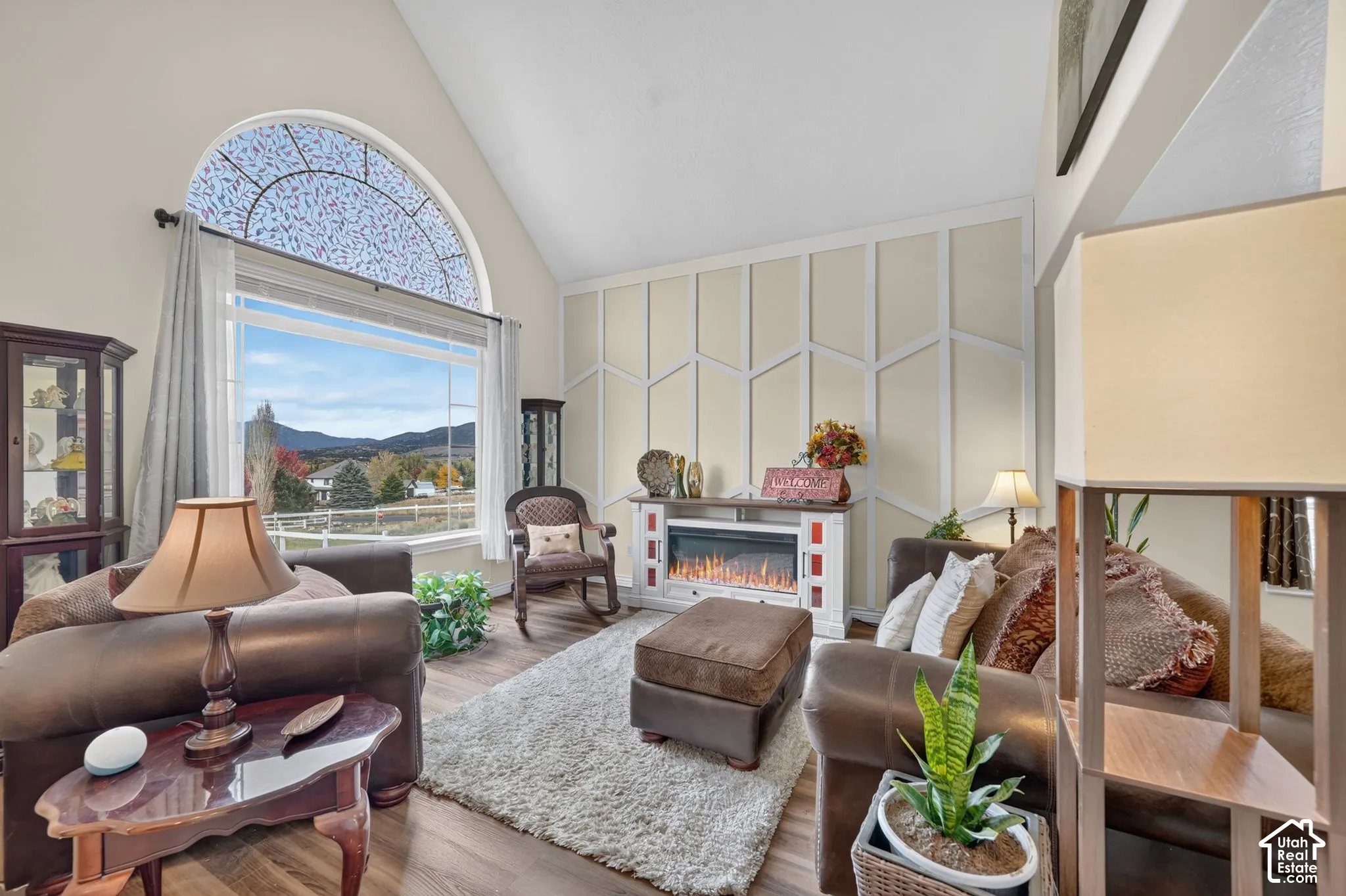 Vaulted ceiling, arched picture window with grid detailing, decorative wall molding, and wood-finish flooring
