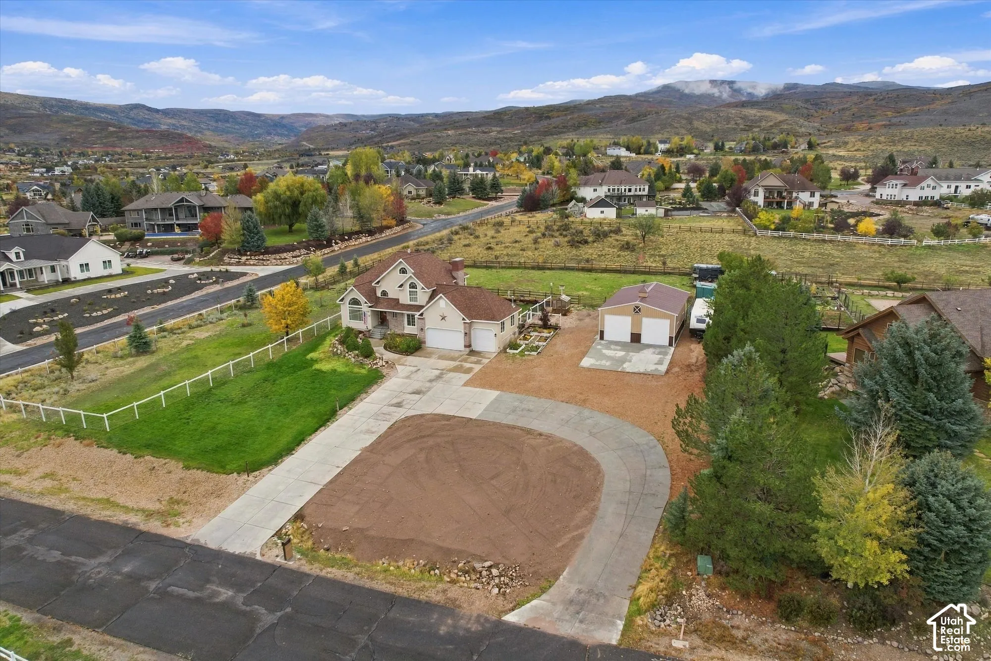 Residential property featuring a multi-level home, a detached garage, a paved driveway, and perimeter fencing, set against a mountainous landscape
