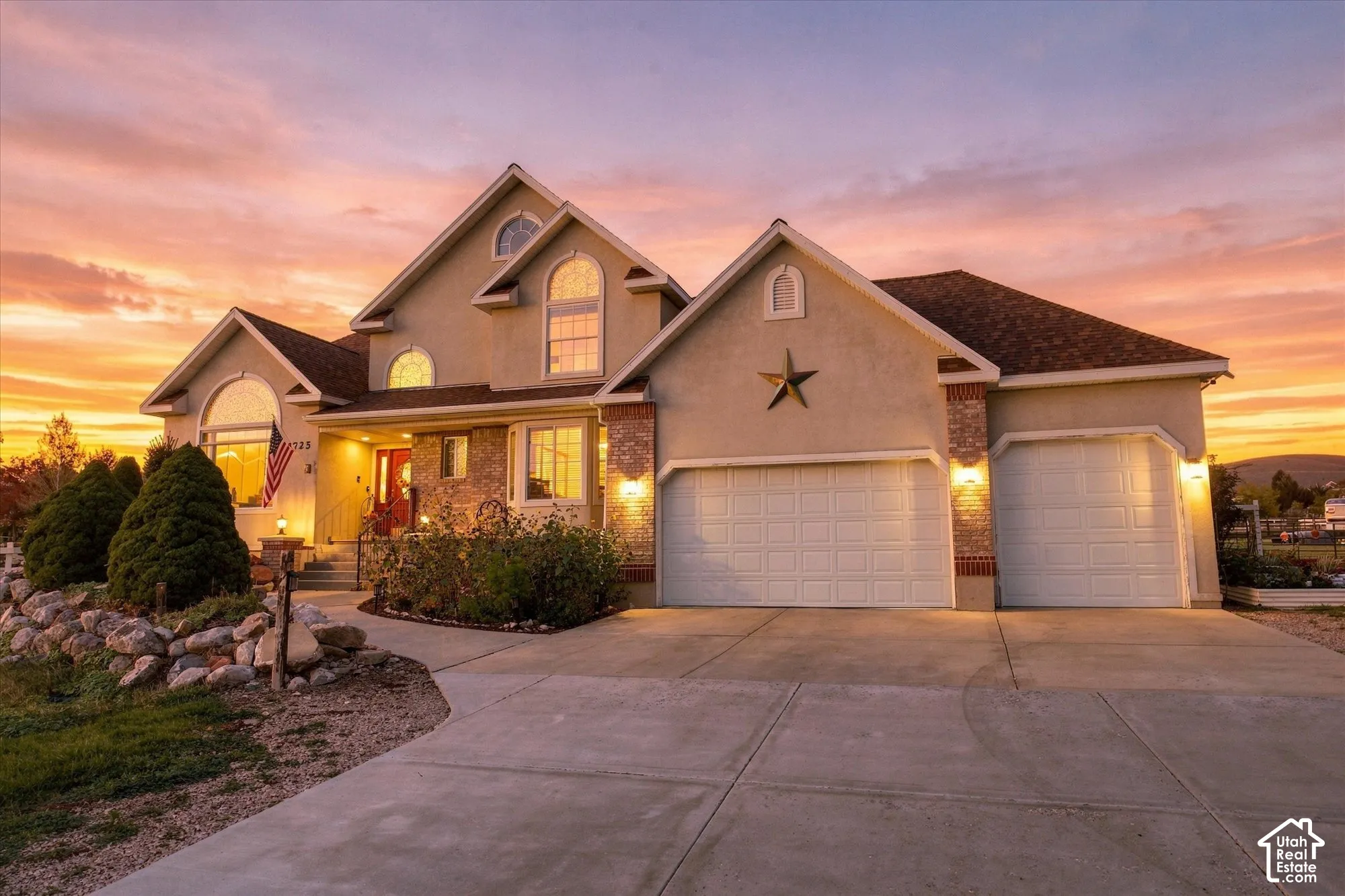 Multi-level exterior featuring stucco and brick masonry, a three-car garage, arched windows, and a paved concrete driveway