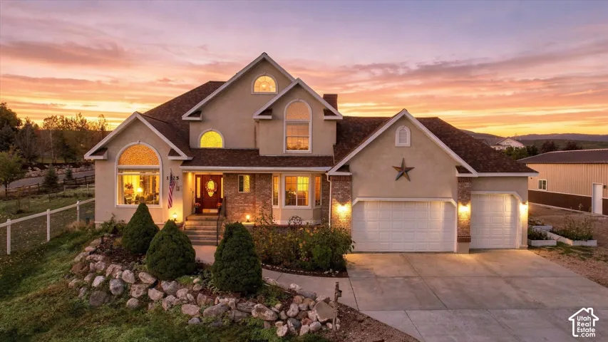 Multi-level stucco exterior featuring stone masonry accents, a three-car garage, arched windows, and a landscaped rock garden