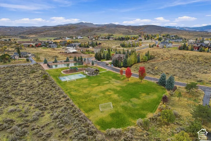 Expansive community grounds featuring a manicured lawn, multi-purpose sports court, paved tennis court, shaded gazebo, and a mountainous landscape backdrop
