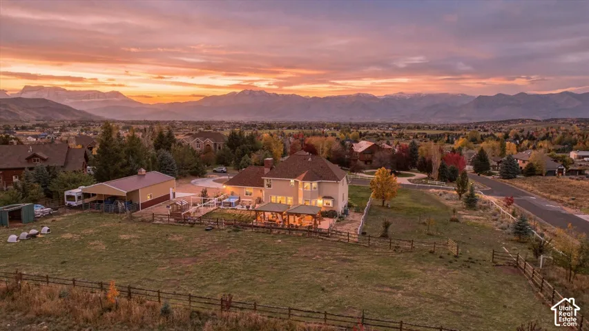 Aerial perspective of a multi-level residence featuring a detached secondary garage, expansive fenced grounds, and a covered patio, set against a mountainous backdrop
