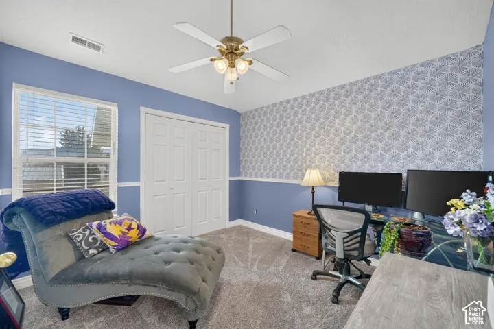 Room featuring patterned accent wall, white-paneled closet doors, crown molding, and a central ceiling fan