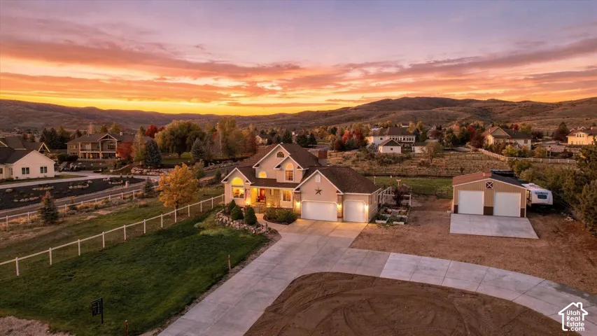 Multi-level residence featuring a pitched shingle roof, attached three-car garage, secondary detached two-car garage, and expansive concrete driveway set against a mountainous backdrop
