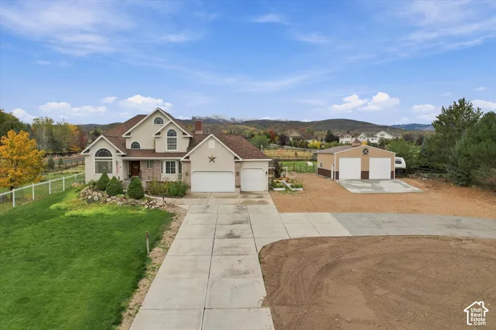 Multi-level residence featuring a brick and stucco exterior, attached three-car garage, detached two-car garage, concrete driveway, and expansive acreage with mature trees