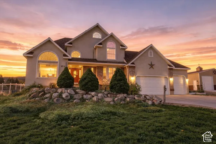 Multi-level exterior featuring stucco and stone masonry, arched window detailing, three-car garage, and tiered rock landscaping
