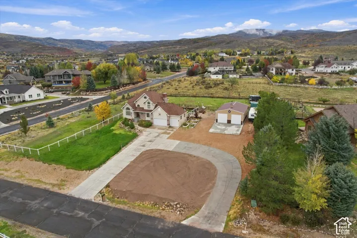 Residential property featuring a multi-level home, a detached garage, a paved driveway, and perimeter fencing, set against a mountainous landscape