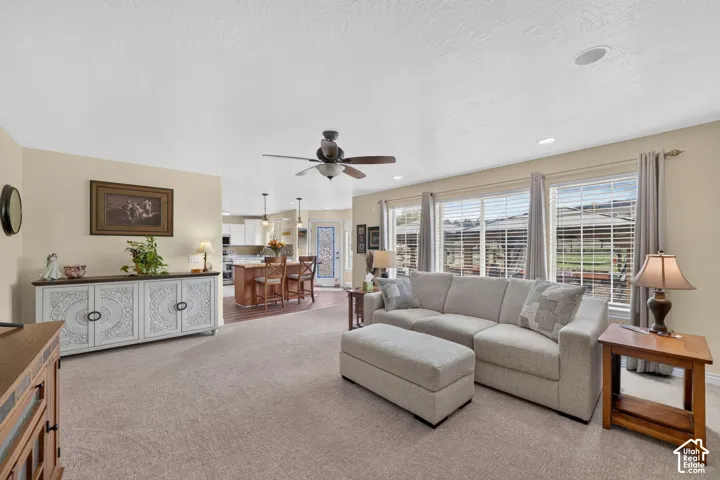 Living space featuring neutral wall tones, recessed lighting, a ceiling fan, and large windows with horizontal blinds