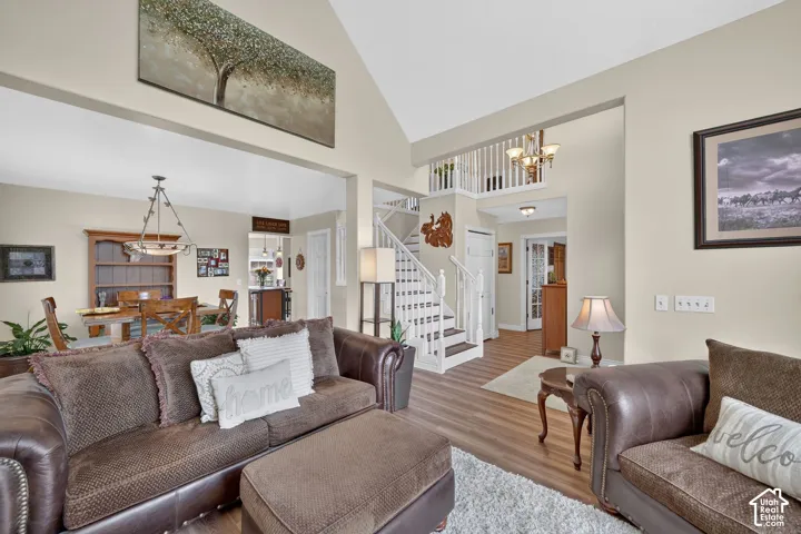 Vaulted ceilings, staircase with white railing, wood-finish flooring, and multi-tier chandelier lighting