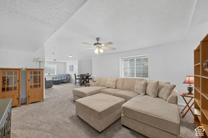 Expansive open-concept living area featuring wall-to-wall carpeting, a ceiling-mounted light fixture with fan, and windows with horizontal blinds