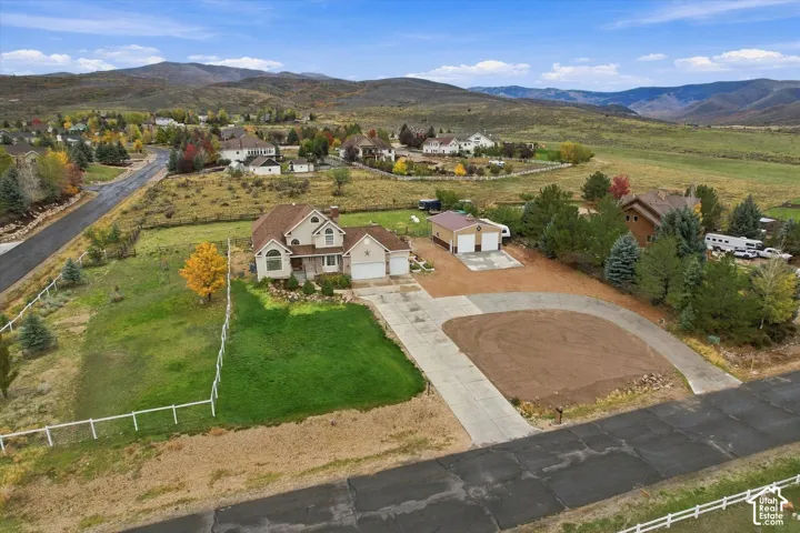 Aerial view featuring a multi-level residence, detached two-car garage, expansive lot with fenced perimeter, and mountainous horizon